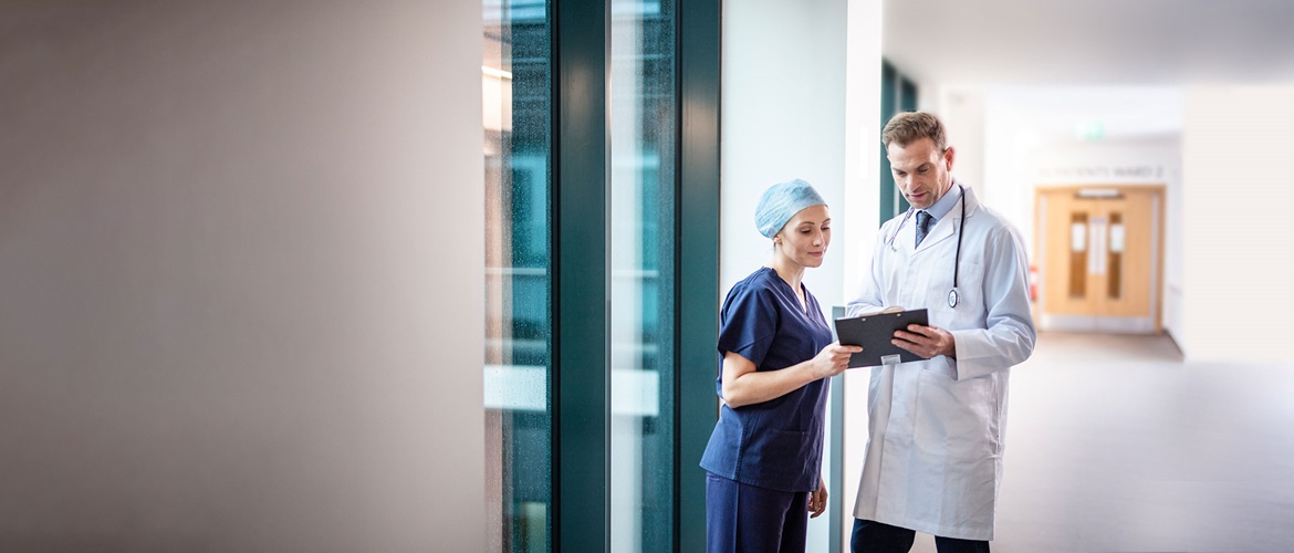 Doktor v bílém plášti se stetoskopem a lékařka v modrém plášti v chodbě nemocnice